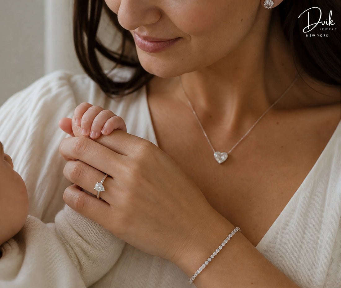 Dvik Jewels featuring a silver heart shaped diamond necklace, pear-cut diamond ring, and a tennis bracelet worn by a mother holding her baby's hand