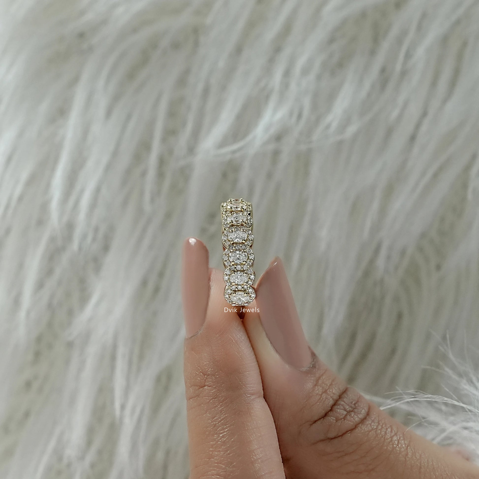 Oval cut eternity band held to show the high-quality gold setting.