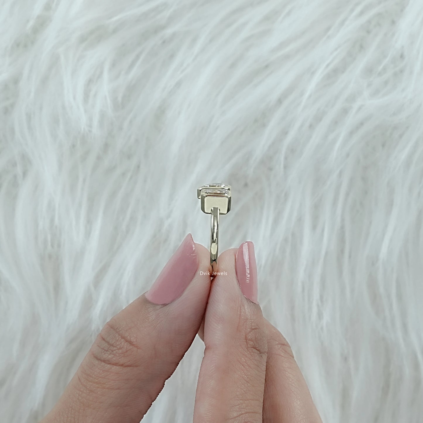 Bezel Set Emerald and Pear Cut Toi Moi Engagement Ring shown from side angle held by woman