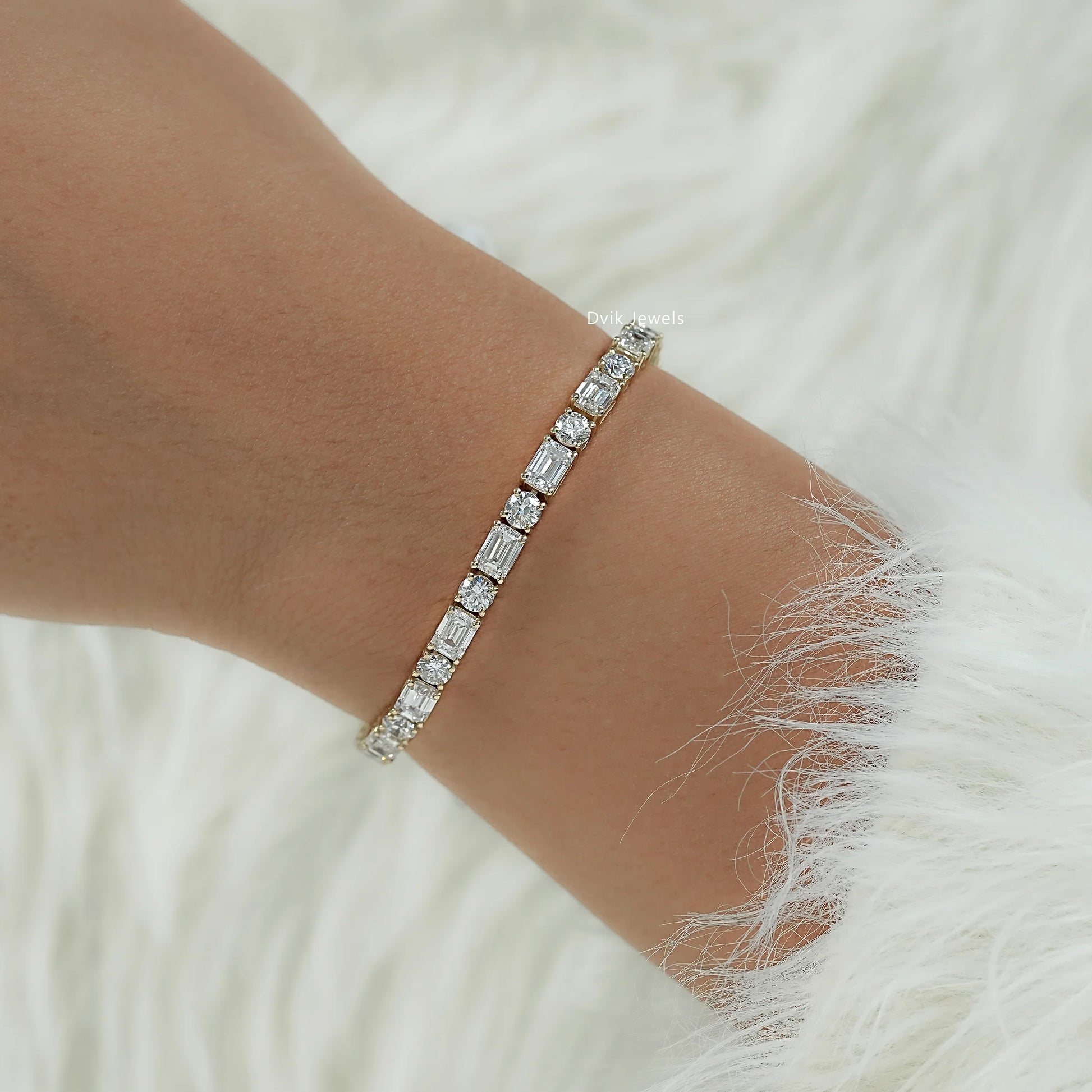 Detailed view of emerald and round diamond tennis bracelet on model hand