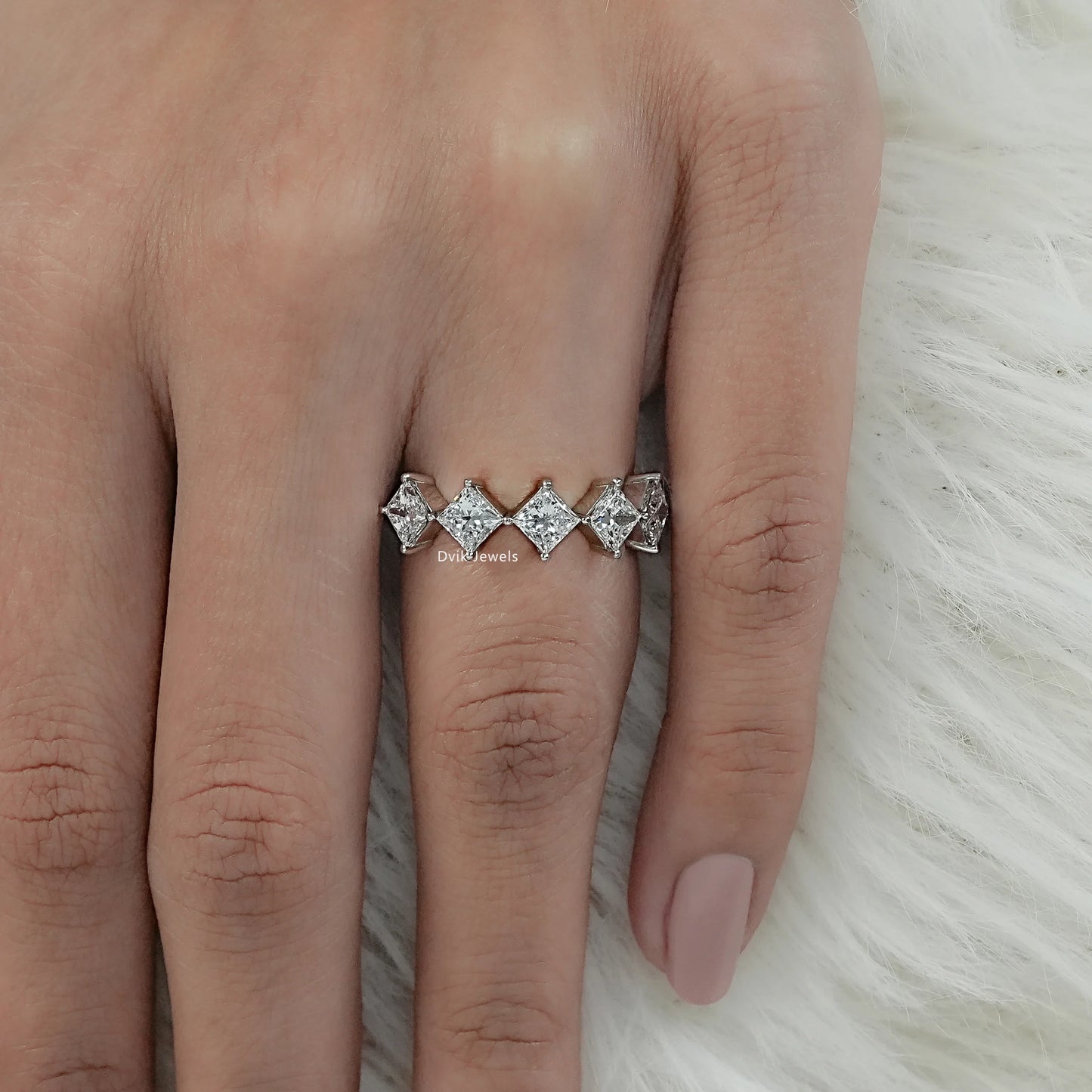 Top view of a princess cut diamond ring 2 carat on finger with white fur background.