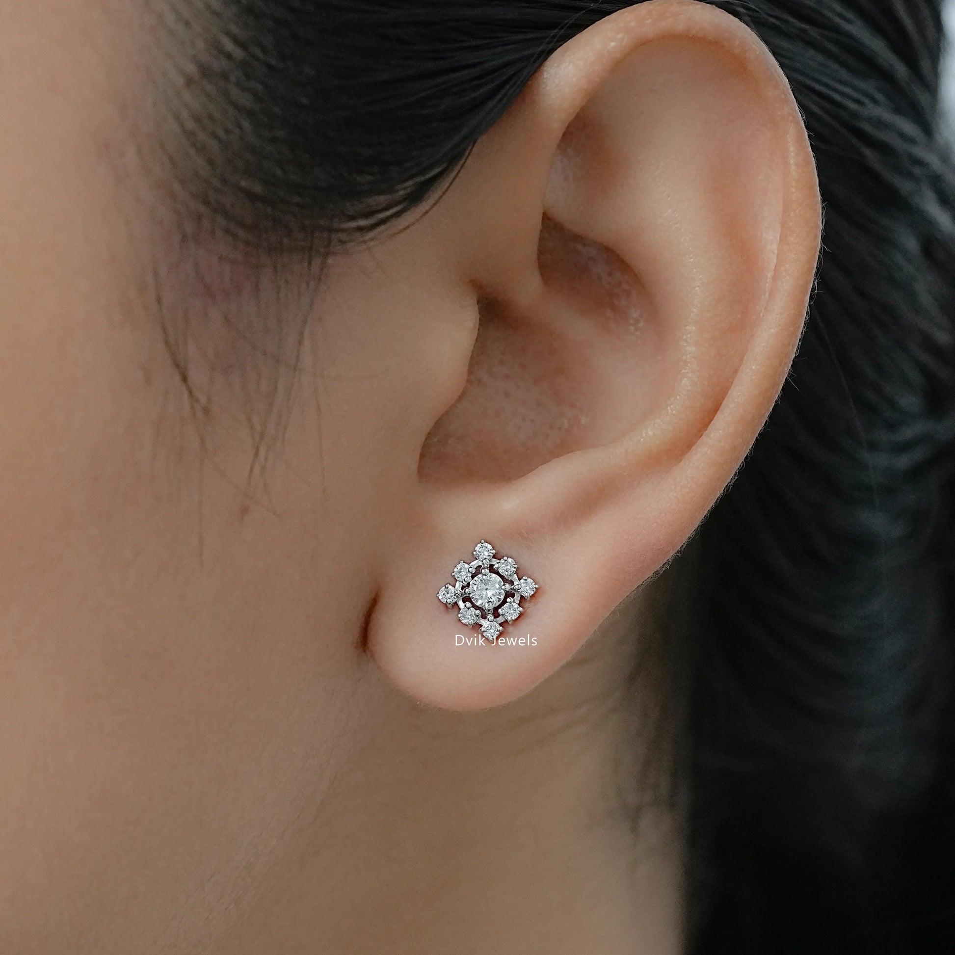 Top view of round diamond halo earrings worn on the ear against a soft background.