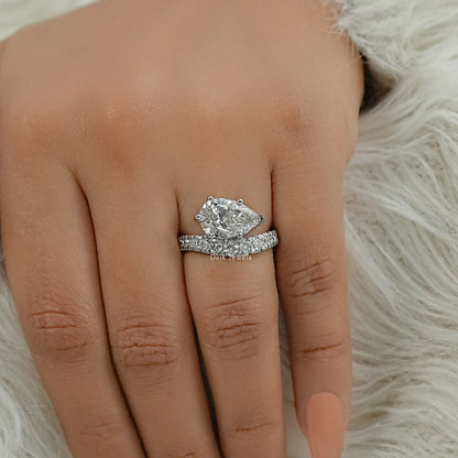 Curved wedding band paired with a pear diamond ring on a hand with nude nails.