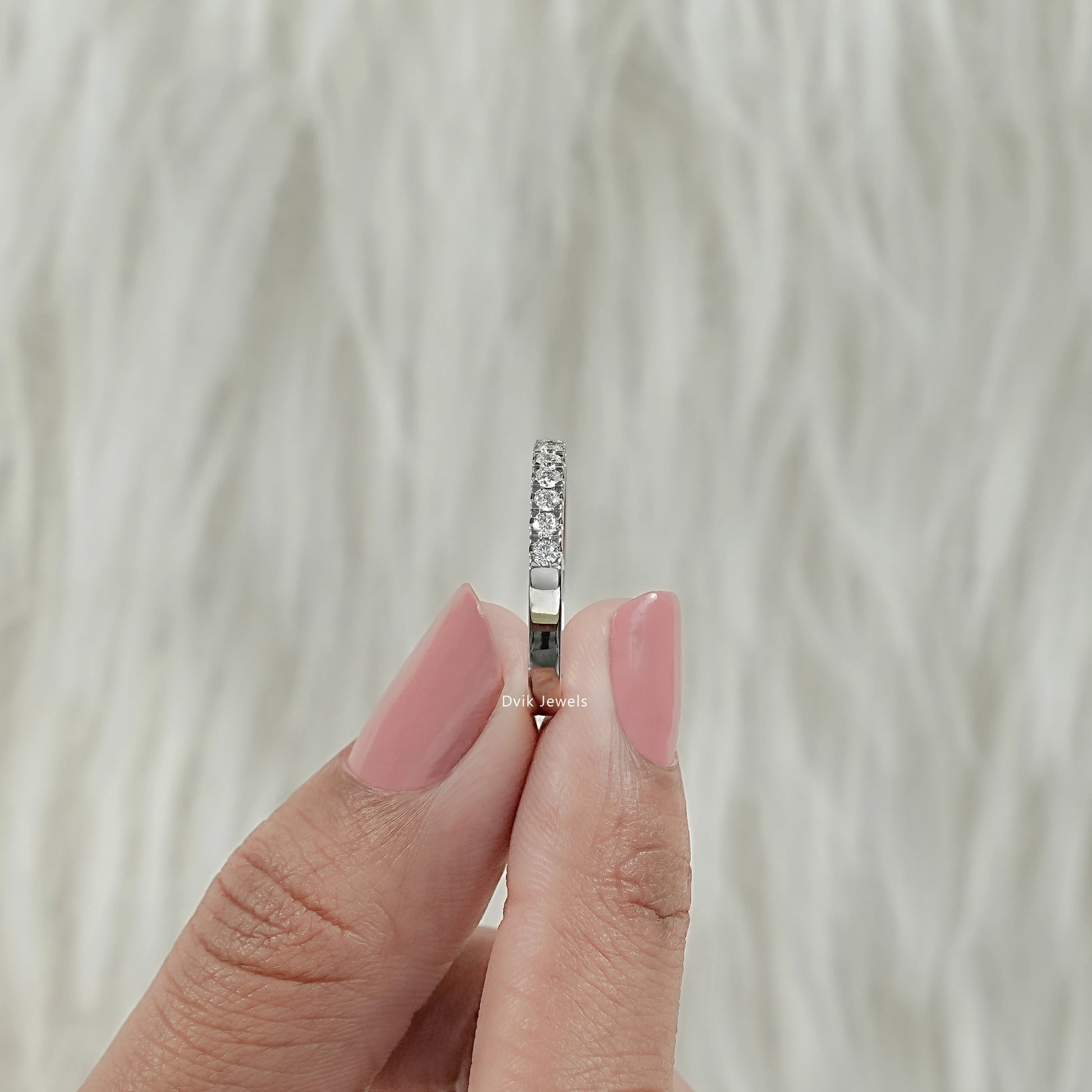 Side view of round diamond eternity band with open gallery holes held by women