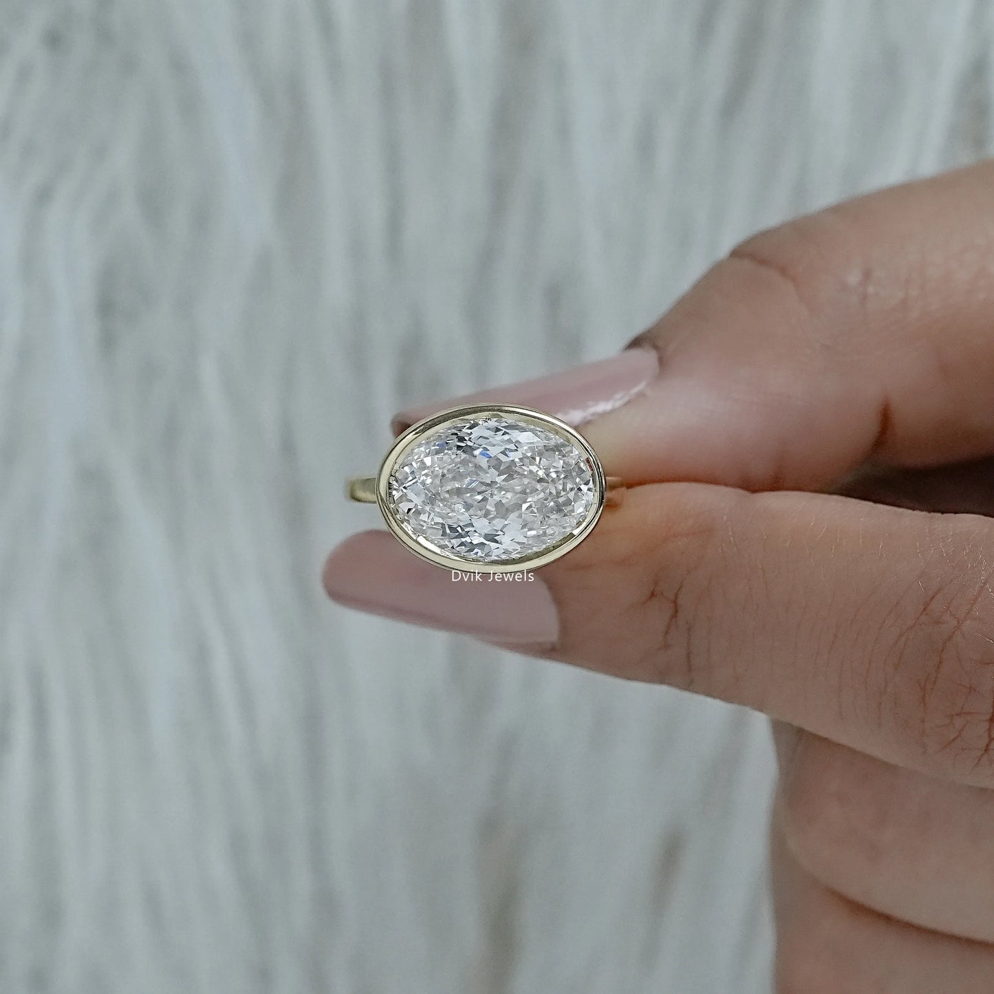 Oval engagement ring with bezel yellow gold solitaire held in hand