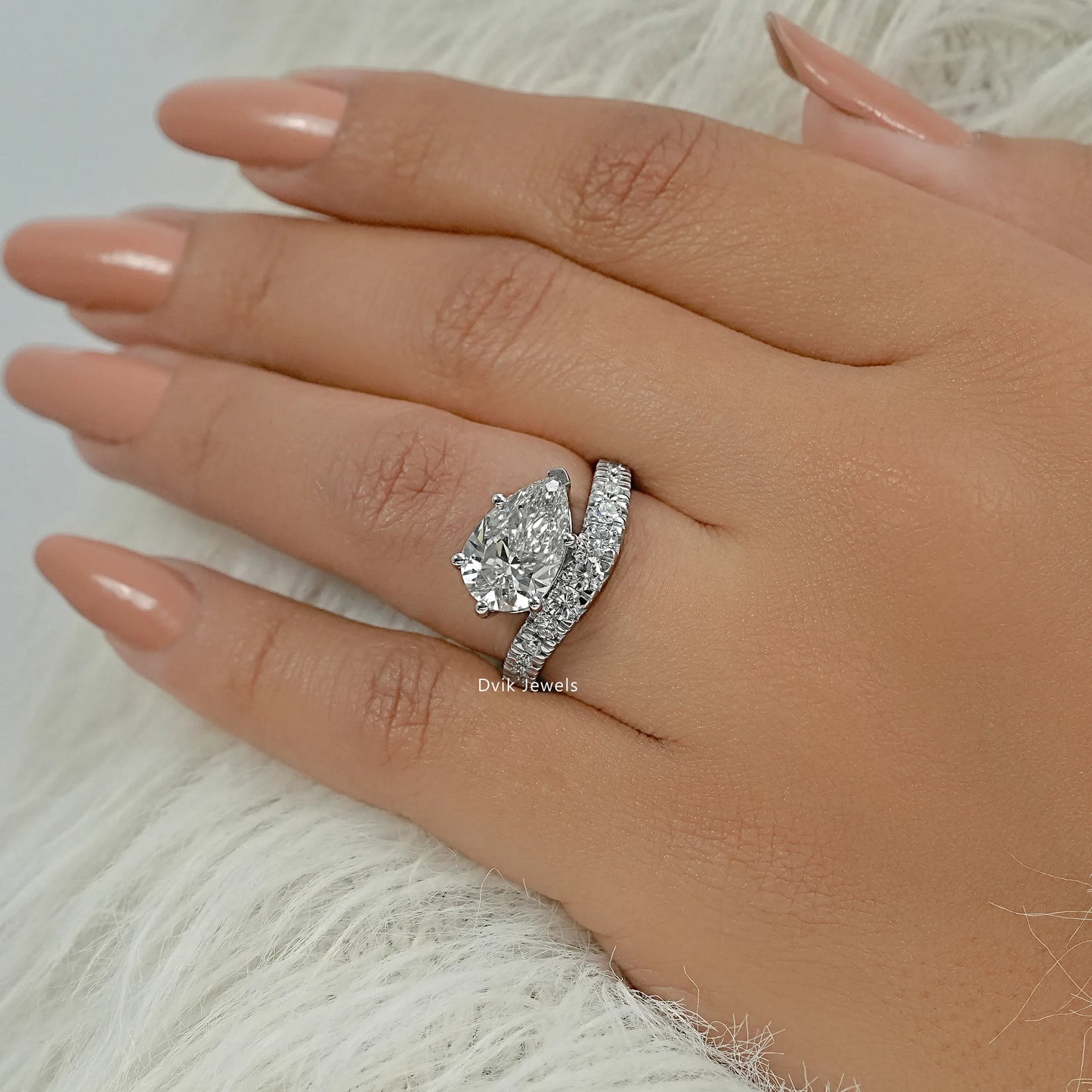 Pear shaped engagement ring in a bypass setting worn on a finger, top view.