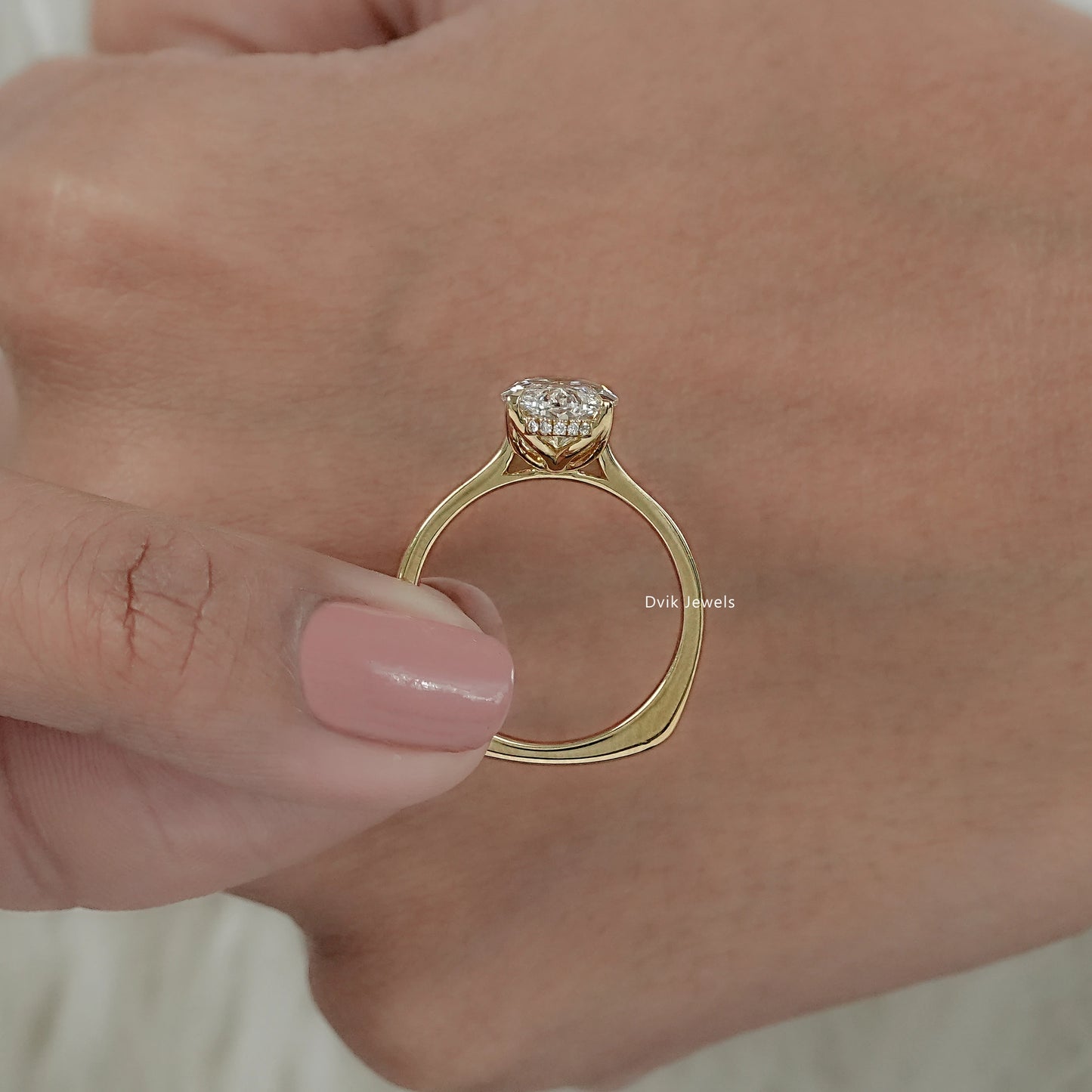 Human fingers hold moval diamond ring to show basket setting