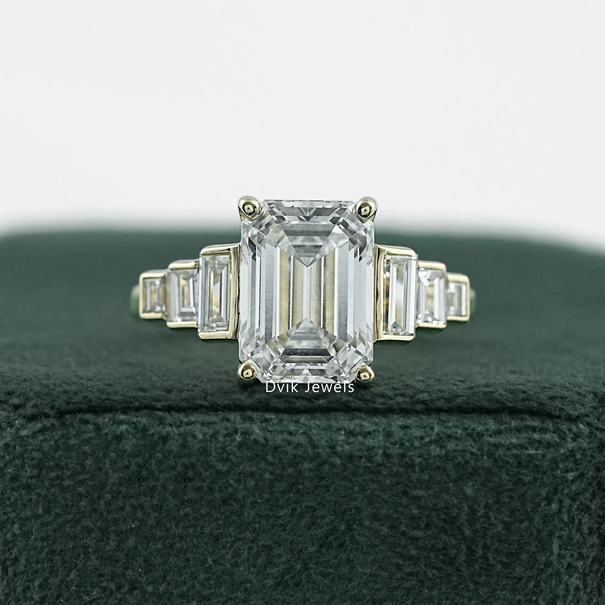 Elongated emerald cut engagement rings in 14k yellow gold on white fabric.