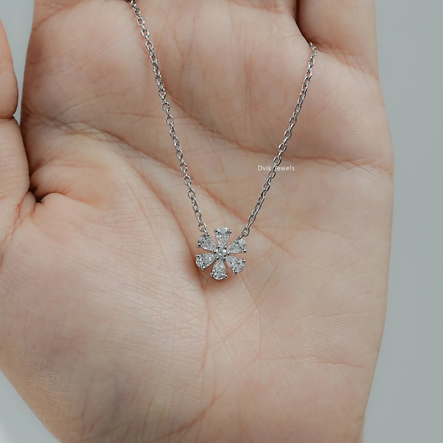 Model hand hold pear and round diamond floral necklace with secure prong setting