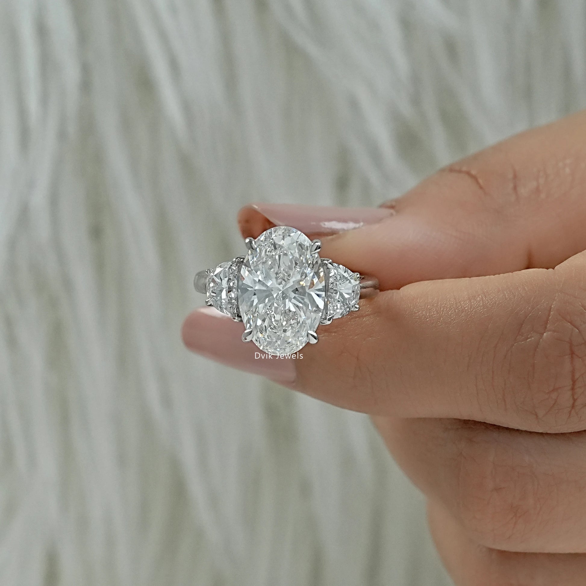 Oval three stone engagement rings held between fingers to show metal detail