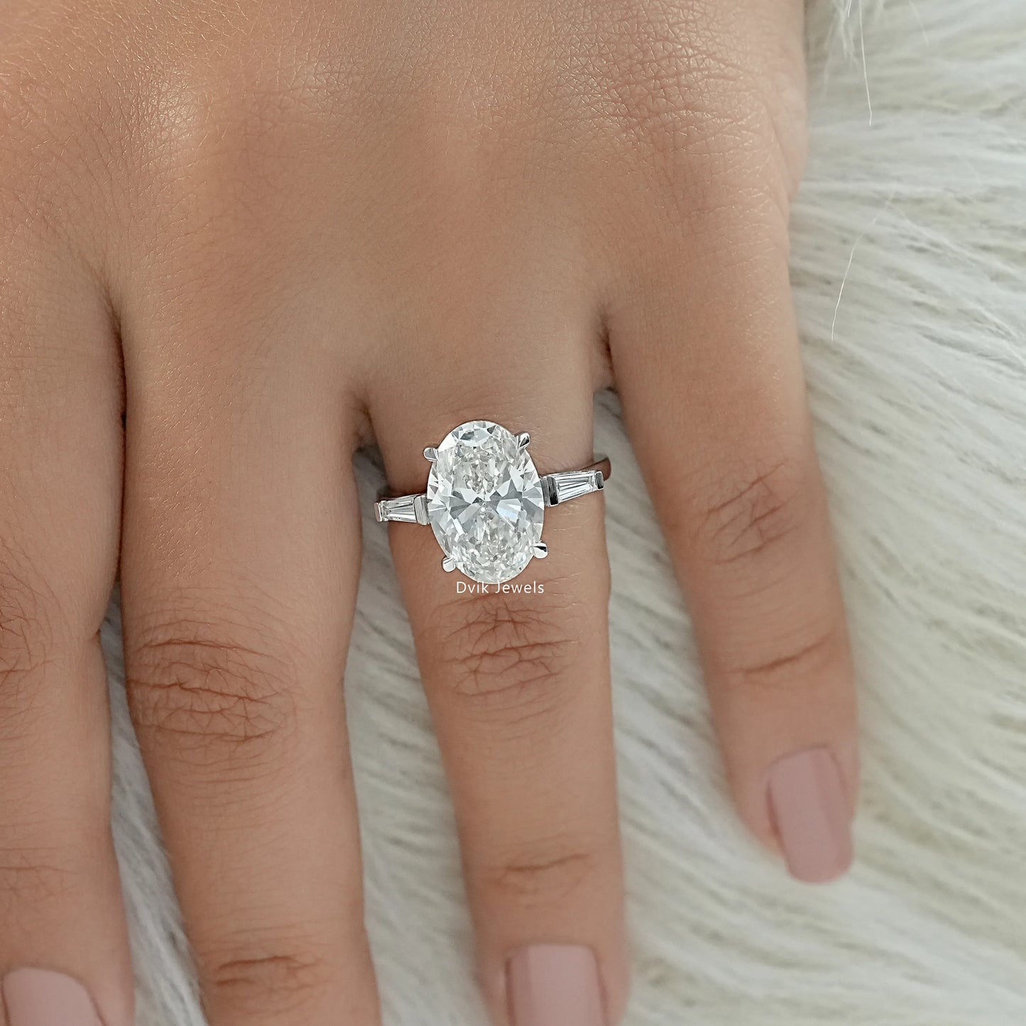 Top view of oval engagement ring with tapered baguette side stones on finger against white fur.