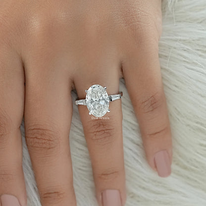 Top view of oval engagement ring with tapered baguette side stones on finger against white fur.