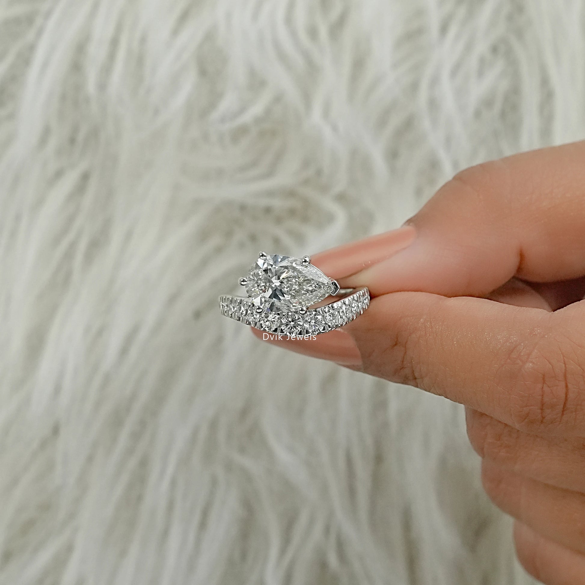 3 carat pear shaped diamond ring with a matching curved band held in hand.
