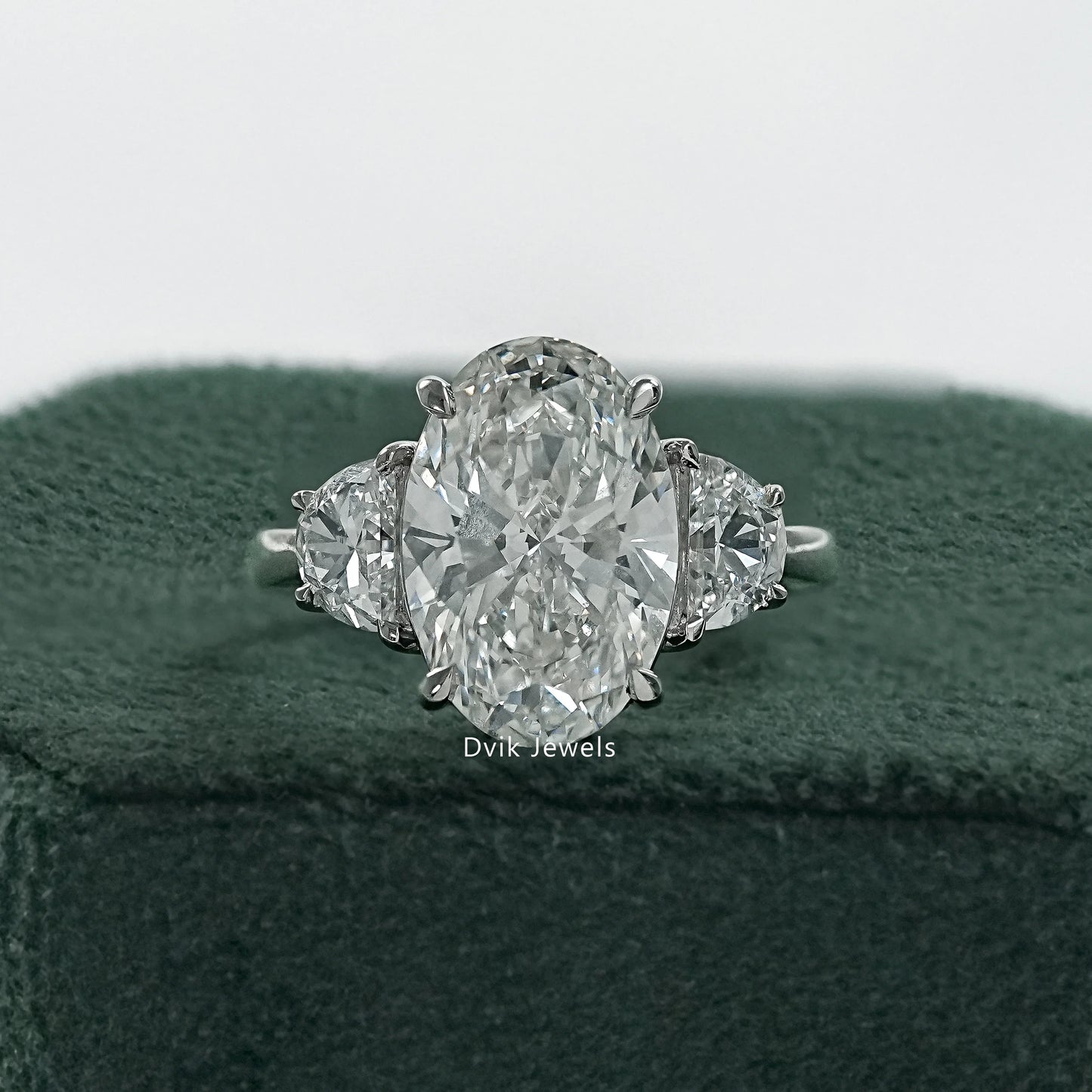 Oval diamond half moon side stones ring held to show the three stone profile