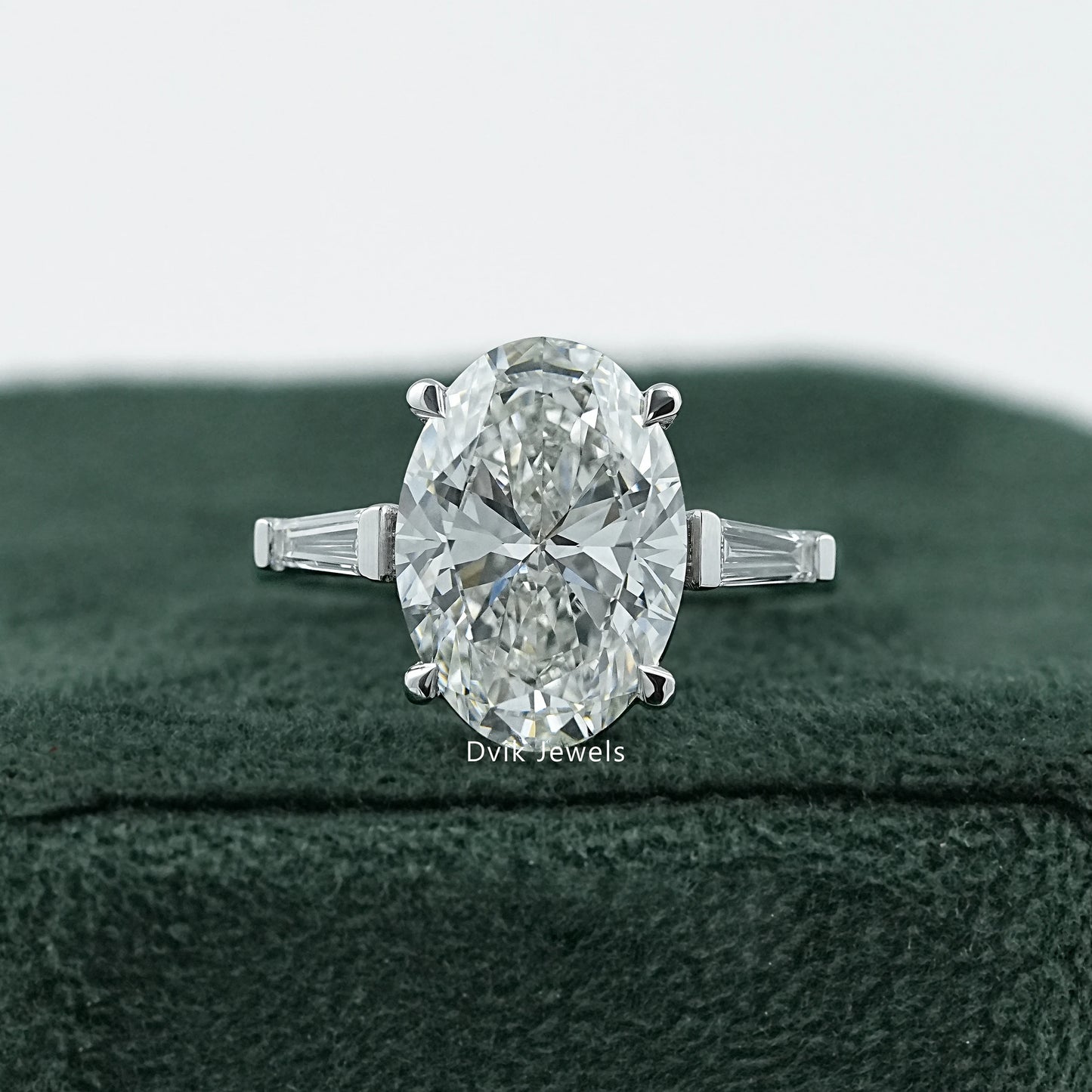 Dvik Jewels Oval Engagement Rings with Side Stones front view placed on dark green velvet.