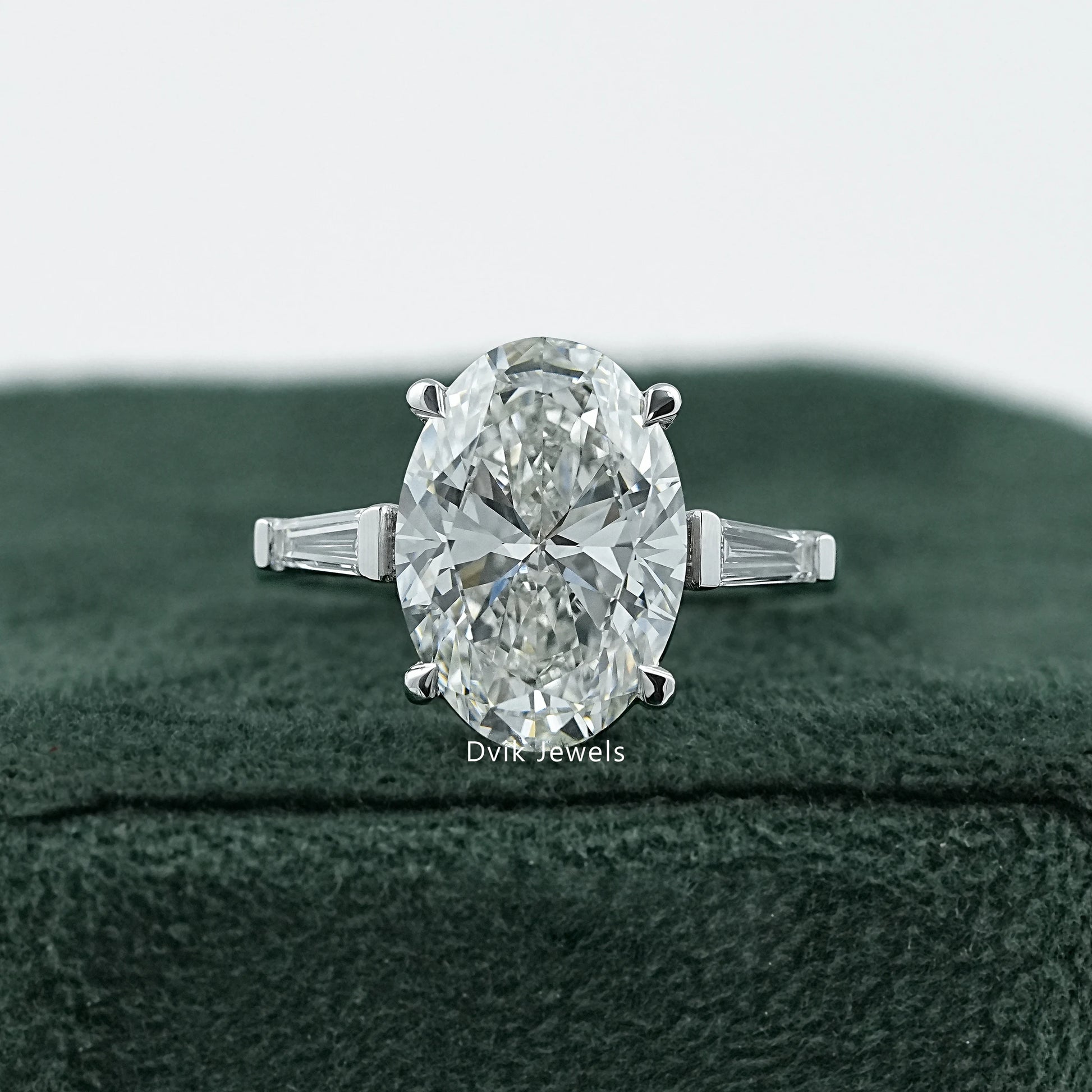 Dvik Jewels Oval Engagement Rings with Side Stones front view placed on dark green velvet.