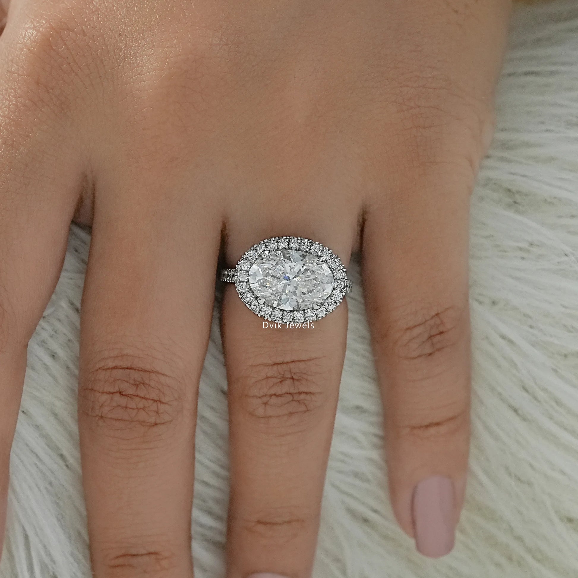 Oval engagement ring with halo worn on a hand to display the brilliant fit