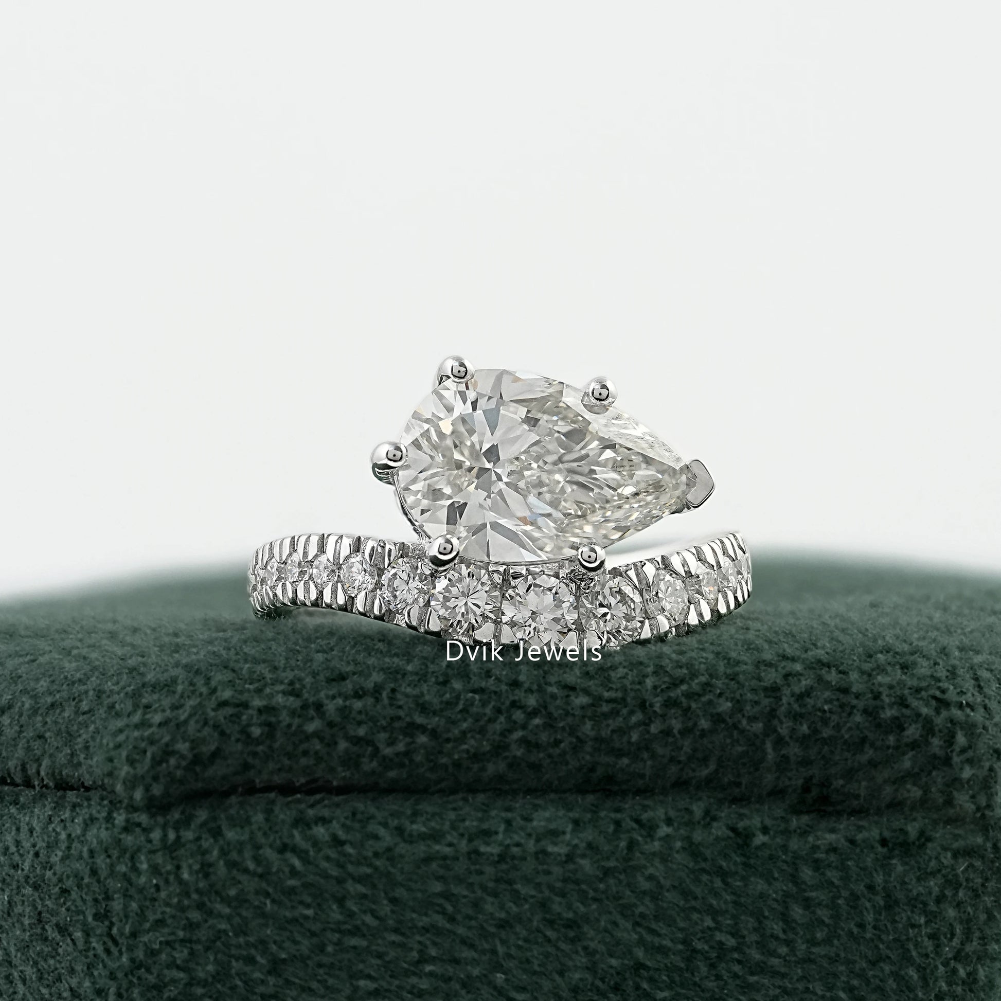 Pear diamond engagement ring on a green velvet box with a curved pavé band.