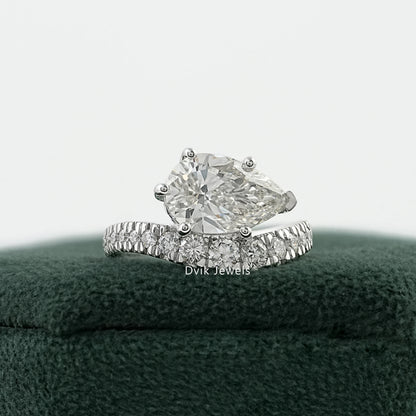 Pear diamond engagement ring on a green velvet box with a curved pavé band.
