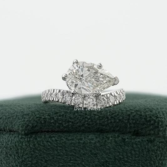 Pear diamond engagement ring on a green velvet box with a curved pavé band.