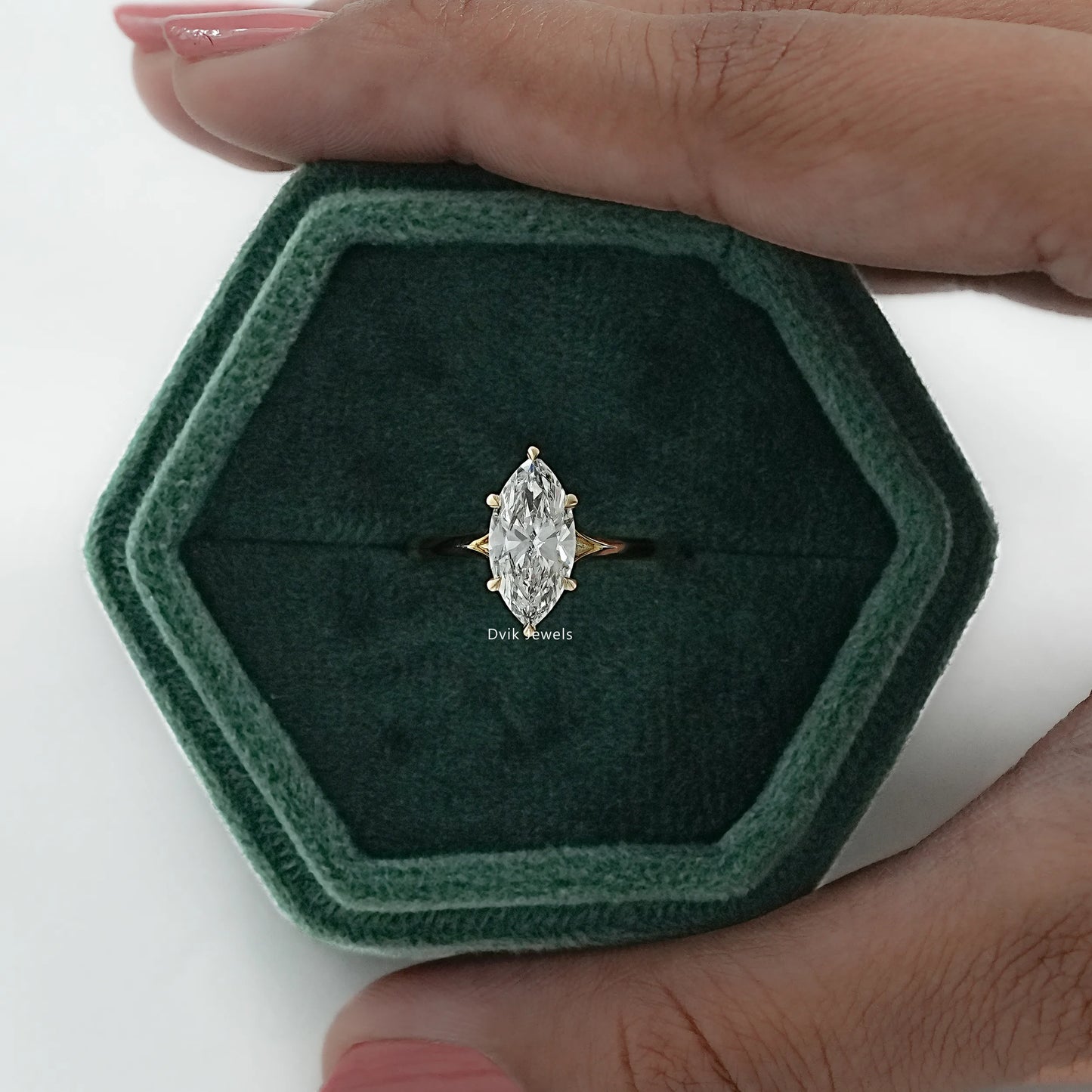 Close-up of a minimalist marquise cut engagement ring held between fingers for stone's brilliance