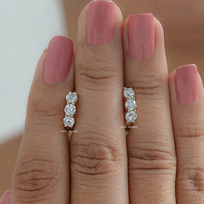 Three stone hoop earrings held between women fingers to demonstrate huggie-style size